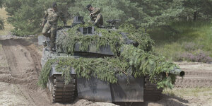 zwei Soldaten auf einem Panzer, der mit Zweigen eines Nadelbaums bedeckt ist