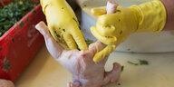 ein Mensch mit gelben Gummihandschuhen stopft ein Huhn mit Kräutern