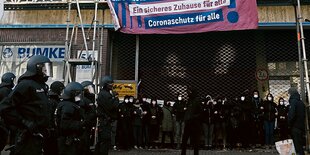 Demonstranten blockieren ein Tor, um sie herum stehen Polizisten.