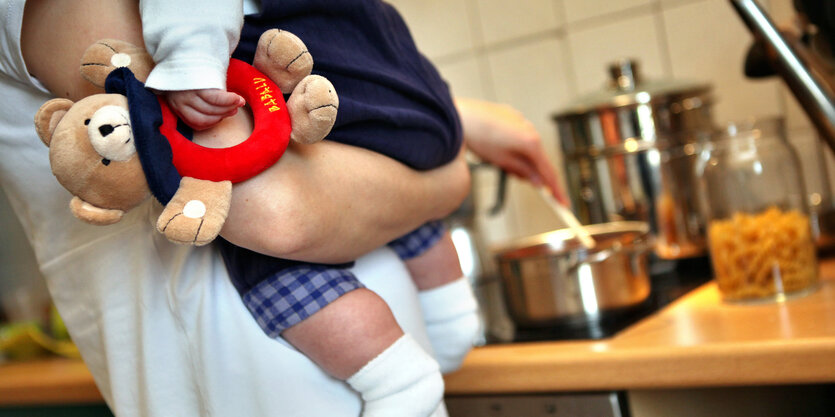 Eine Frau hält beim Kochen ein Kind im Arm