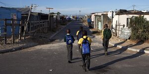 Vier Jungen tragen Schulrucksäcke und gehen eine Straße entlang