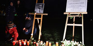 Kerzen und Blumen werden im dunkeln vor einer gedenktafel abgelegt