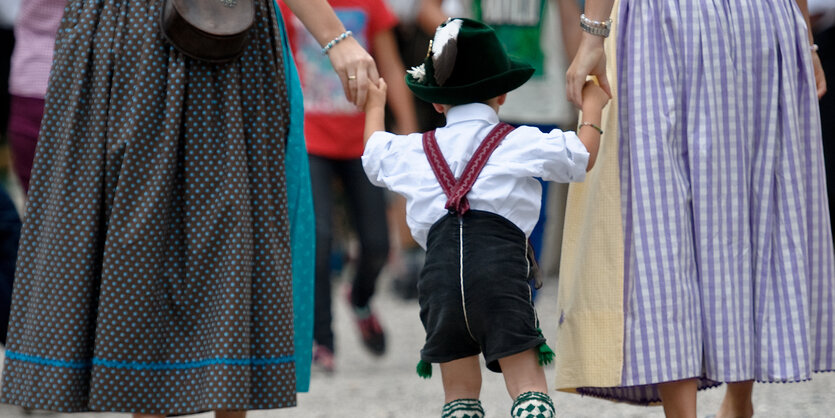 Ein Kind in Lederhosen hält die Hände von zwei Frauen