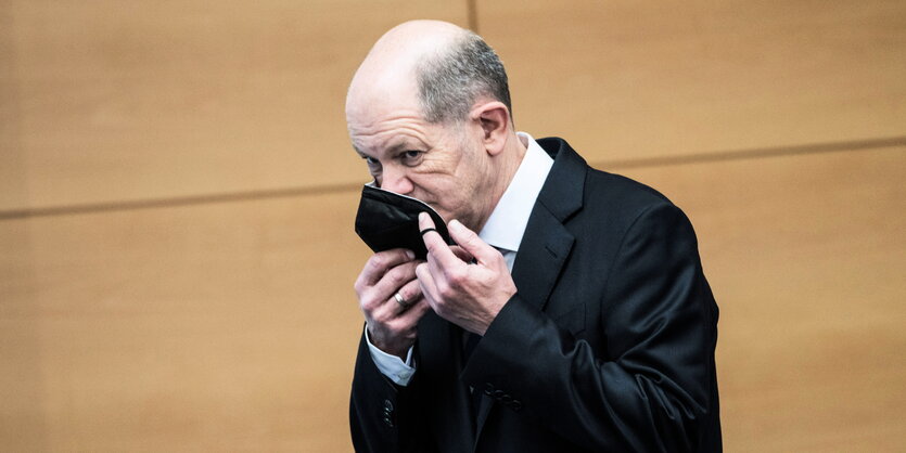 Olaf Scholz hantiert mit seiner Maske.