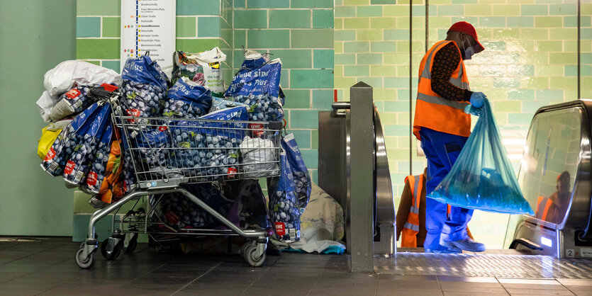 Ein vollkommen überfüllte Einkaufswagen steht am Rande eine Rolltreppe - dahinter liegt eine Decke am Rande einer Rolltreppe