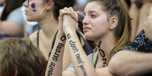 Eine Frau mit Parolen auf den Armen weint, eine andere hat ein Frauenzeichen ins Gesicht gemalt