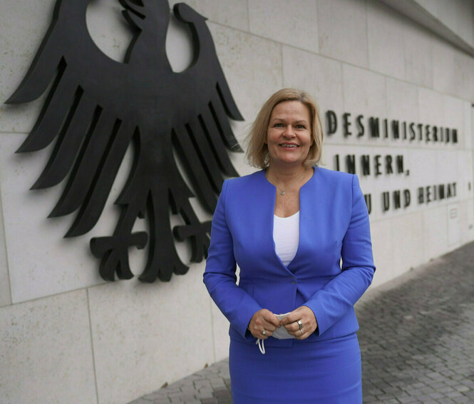 Nancy Faeser steht im blauen Kostüm vor dem Bundesinnenmisterium