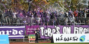 Fans von TeBe Berlin werfen mit lila-weißem Konfetti und Luftschlangen bei einem Fußballspiel