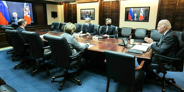 Präsident Biden sitzt mit MitarbeiterInnen an einem langen Tisch, Putin ist per Video zugeschaltet