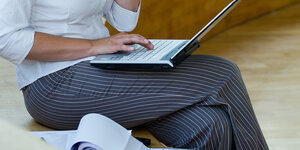 Eine Frau in Geschäftskleidung tippt auf einem Laptop, vor sich einen Aktenordner.