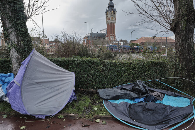 Zwei Zelte am Wegesrand, im Hintergrund das Rathaus von Calais und Räumumgsfahrzeige der Polizei