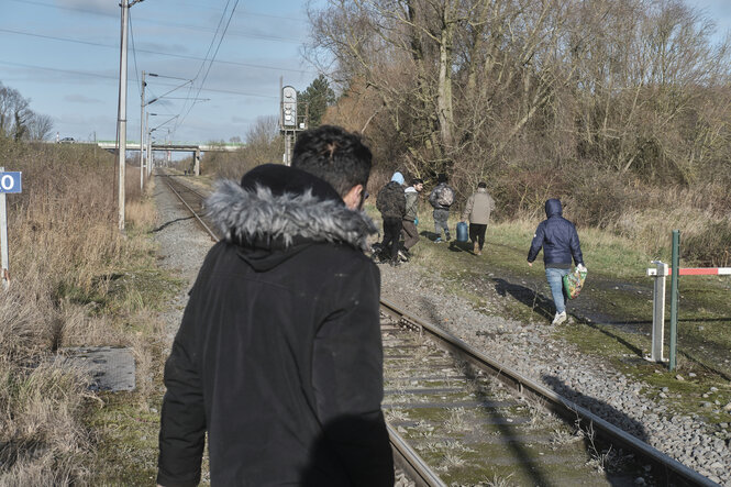 Personen in Winterkleidung laufen Schienen entlang