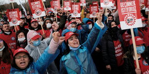 Männer und Frauen mit roten Protestplakaten recken die Fäuste