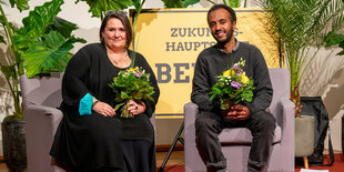 Zwei Menschen mit Blumen sitzen auf Stühlen