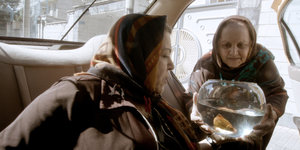 Zwei Frauen mit einem Goldfisch im Glas steigen in ein Taxi ein
