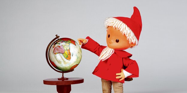 Die Fernseh-Figur Sandmännchen zeigt auf einen Globus.