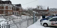 Ein altes Gebäude, Schnee und Polizisten hitner einem Zaun