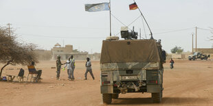 Jeep mit einer deutschen Flagge und einer blauen UN Fahne fährt auf einer sandigen Strasse