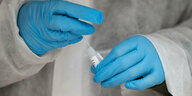 Zwei Hände in blauen Handschuhen stecken ein Wattestäbchen in ein Röhrchen mit Testflüssigkeit.