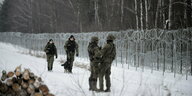 Soldaten patrouilieren mit einem Hund an einem Grenzzaun im SChnee