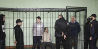 Männer in einem Käfig im Gerichtssall, bewacht von Sicherheitskräften