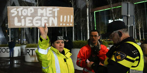 Ein Politizist überprüft eine Demonstrantin, die ein Plakat hochhält: Stop met Liegen - Hört auf zu Lügen