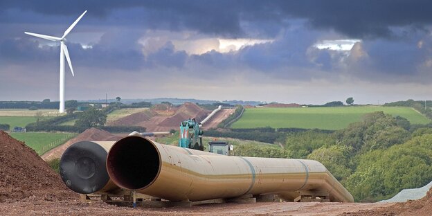 Baustelle einer Gaspipeline, dicke röhren in aufgewühlter Erde, grüne Landschaft, ein Windrad