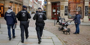 Polizisten und Ordnungsamt gehen in einer Einkaufszone, eine Frau mit Kinderwagen schaut auf die Ordnungskräfte