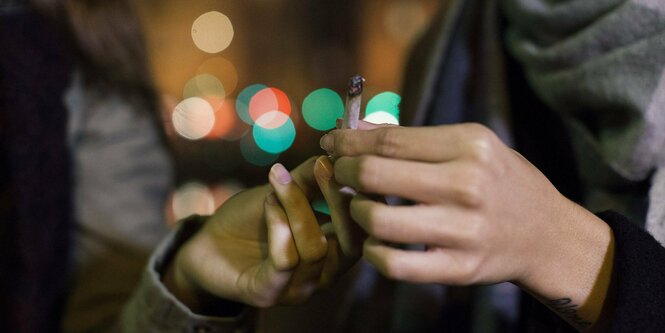 Zwei Personen reichen einen Joint von Hand zu Hand