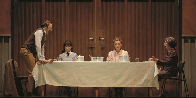 Ein Mann und drei Frauen sitzen an einer Tafel und essen Mittag: Szenenfoto aus der Oper "Katja Kabanowa" an der Komische Oper Berlin