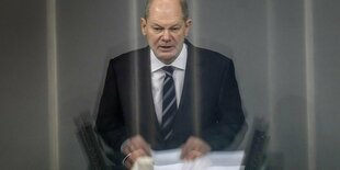 Kanzler Olaf Scholz bei einer Rede im Bundestag, Licht wird an einer Scheibe reflektiert.