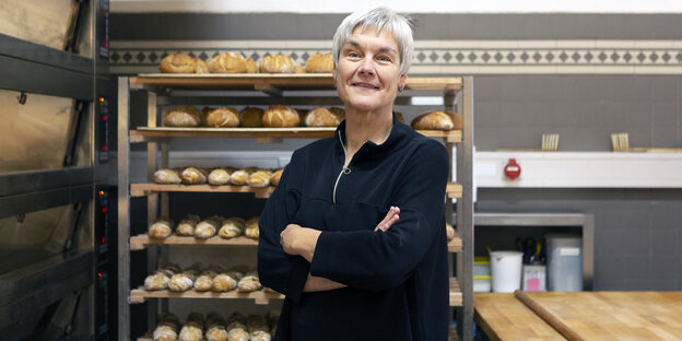 Bäckermeisterin Christa Lutum steht in ihrer Backstube, im Huntergrund Regale mit Brot und Brötchen
