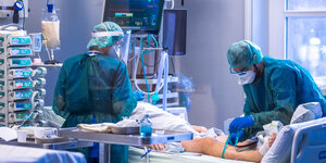 Zwei Intensivpfleger versorgen einen Patienten auf einer Intensivstation.
