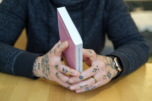 Detailaufnahme von Händen mit Tattoos die ein Buch halten