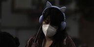 Junge Frau mit Kopfhörern und Nasen-Mund-Schutz hört mit geschlossenen Augen Musik
