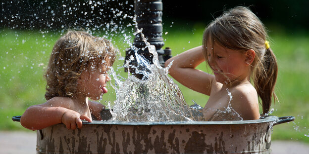 Zwei Kinder sitzen in einem Bottich voll Wasser