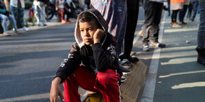 Ein Junge sitzt auf der Straßen, den linken Arm aufs Bein gestützt