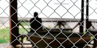Hinter einem Zaun sitzt ein Asylsuchender vor einem Wohnblock im Ankerzentrum Schweinfurt.