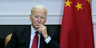 Joe Biden hört an einem Pult zu, um ihn herum die US-amerikanische und die chinesische Flagge