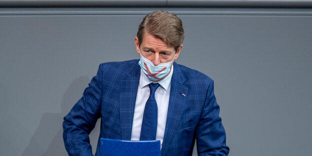 Der Bundestagsabgeordnete Karsten Hilse trägt eine OP-Maske mit draufgemaltem roten Kreuz unter der Nase