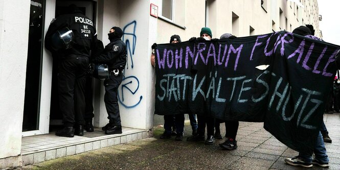 Aktivisten stehen mit einem Transparent vor einem EIngang mit Polizisten