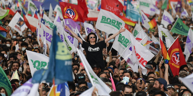 Blick auf eine Menschenmasse, in der Anhänger des frischgewählten Boric in Chile seinen Wahlsieg feiern. Viele schwenken Fahnen, ein Mann mit Sonnenbrille ragt heraus und reckt die Arme in die Höhe