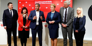 Menschen stehen auf einem Podium und schauen in die Kamera