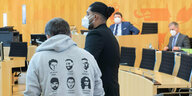 Said Etris Hashemi kommt als Zeuge in den Untersuchungsausschuss im Landtag Hessen, neben ihm trägt ein Mann ein Sweatshirt mit Gesichtern und namen der Opfer des Hanau-Anschhlags