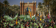 Katalanische Fahne, grüne Hände und Transparente werden von einer Menschenmenge zwischen Palmen hochgehalten