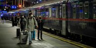 Passagiere mit Gepäck stehen abends vor dem Nachtzug auf dem Bahnstaig