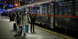 Passagiere mit Gepäck stehen abends vor dem Nachtzug auf dem Bahnstaig