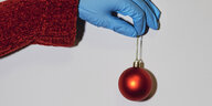 Eine Hand mit blauem Gummihandschuh hält eine rote Weihnachtskugel