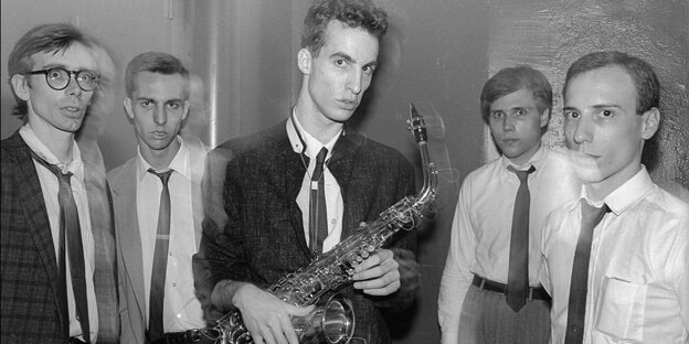 Schwarz-weiß Foto von fünf Männern. Der in der Mitte hält ein Saxophon