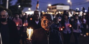 Ein Mannhält eine Kerze. Im Hintergrund eine Masse an Menschen mit Flaggen und Kerzen
